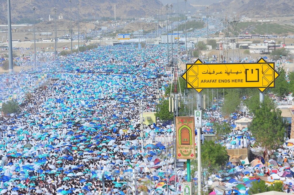 A sign marking the boundary of Arafat and pilgrims gathering for the standing