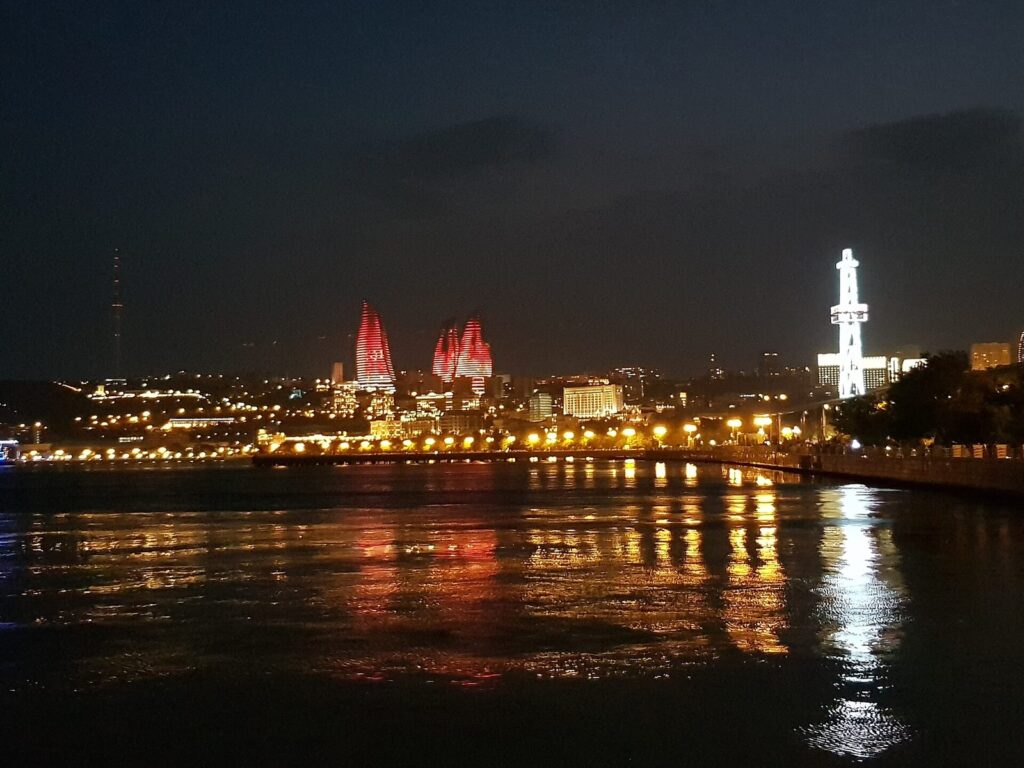 Bakü Bulvarı'ndan gece görünümü, kırmızı ışıklı Alev Kuleleri ve Hazar'a yansıyan ışıklar